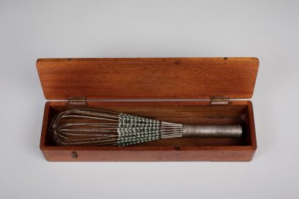 Old whisk decorated with woven ribbon in wooden box